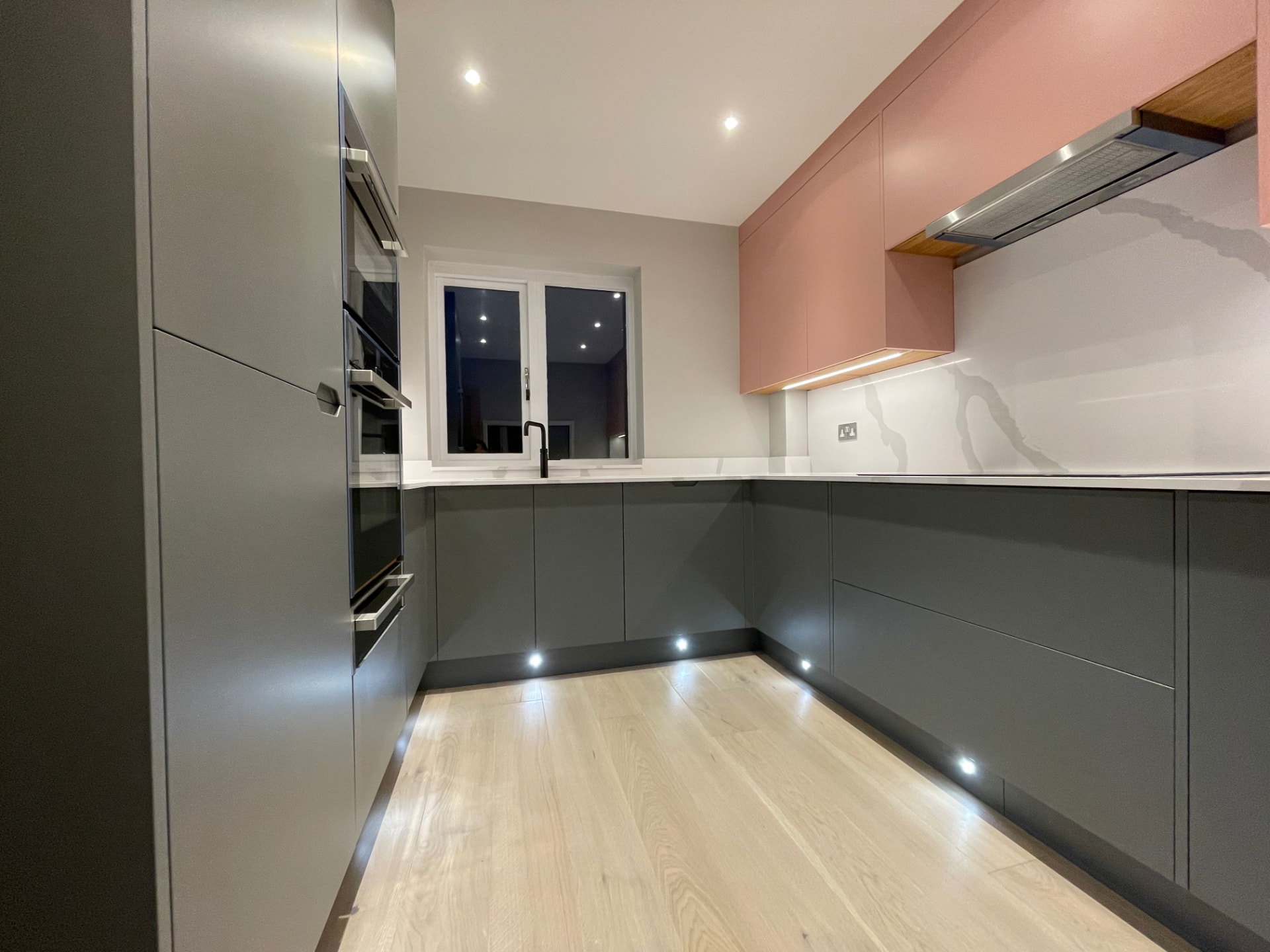Handleless graphite kitchen with blush pink wall units and marble-effect worktops