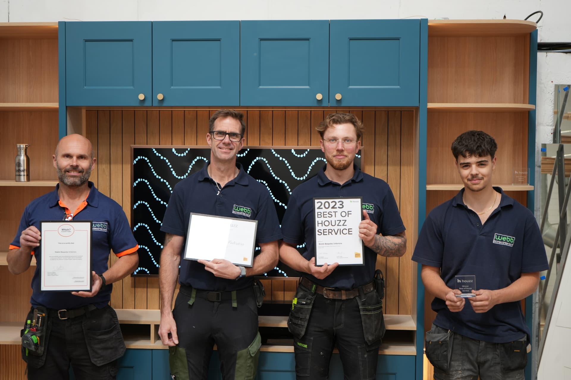 The Webb Bespoke Interiors team — four craftsmen in branded polo shirts holding their Which? Trusted Trader and Houzz awards in front of a bespoke fitted media unit