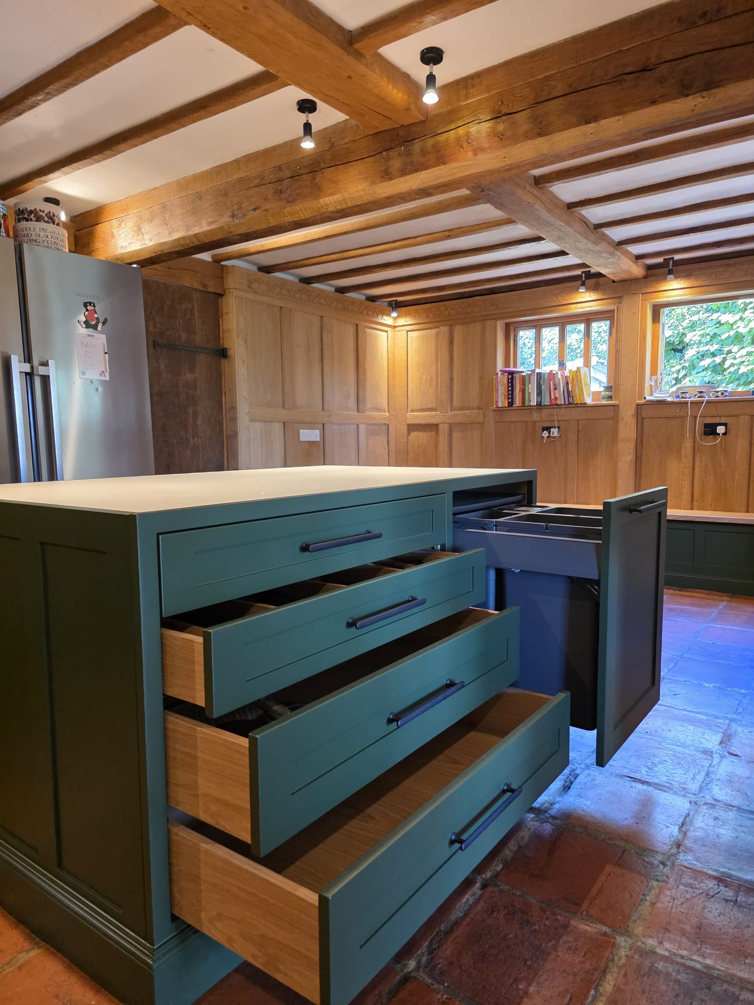 Bespoke painted kitchen island in teal and green with oak-lined drawers under exposed beams