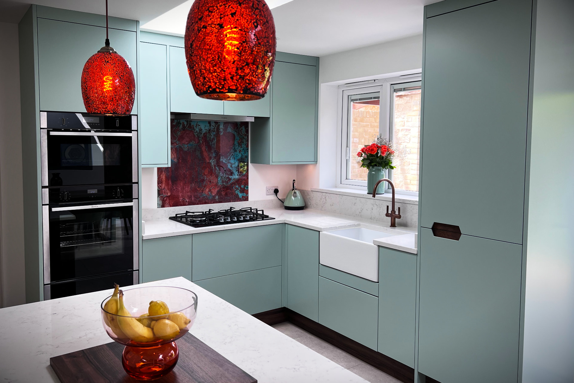 Soft green handleless kitchen with copper splashback, brass tap and marble worktops